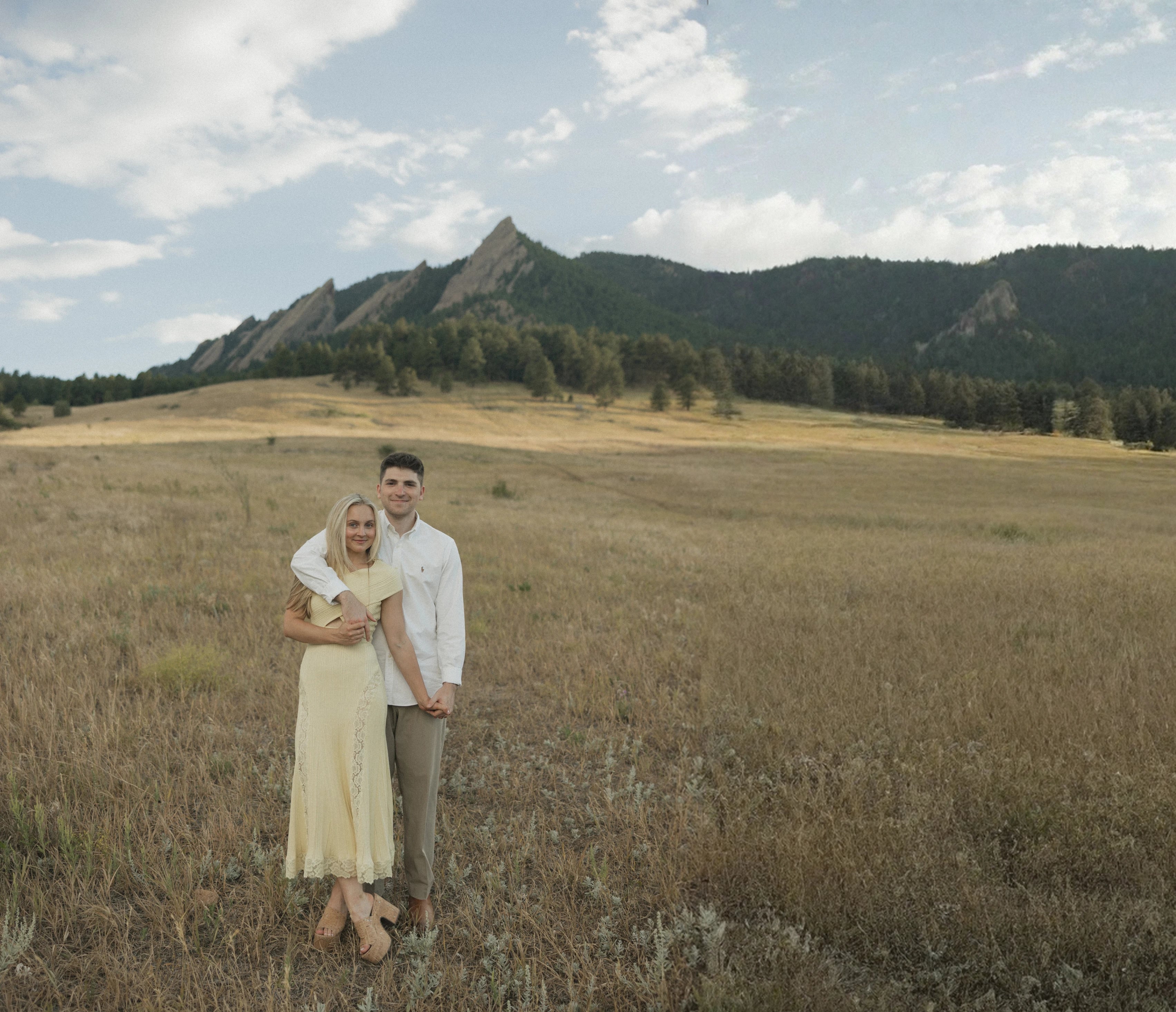 Anna and Emmett standing in a golden field below the Flatirons in Boulder